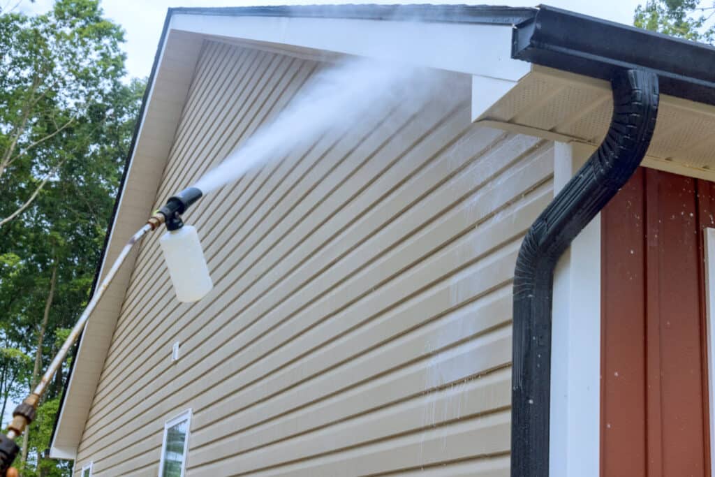 Water soap cleaner is sprayed onto siding houses by a service worker, employing high pressure nozzles.